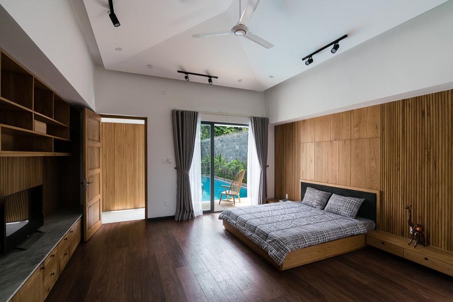 Phòng ngủ chính với ô cửa nhìn ra hồ bơi. Nội thất gỗ tạo cảm giác ấm áp.