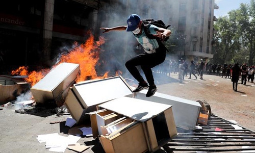 Người biểu tình nhảy lên chướng ngại vật trên đường phố ở thủ đô Santiago, Chile hôm 22/10. Ảnh: Reuters.  